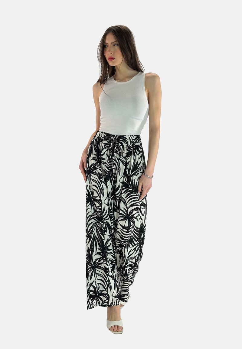 Zwart-witte palmenbladpatroon wijde broek met een elastische tailleband, gecombineerd met een aansluitend wit tanktop en lichte hakken.