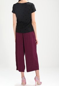 Top negro de manga corta con patrón de estrellas, combinado con pantalones de barga anchos y texturizados. La modelo lleva puestas unas rosas de tacón alto adornadas.