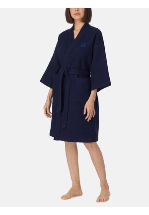 Femme portant un peignoir texturé nid d’abeille bleu marine, longueur genou, manches larges, poches avant et ceinture nouée.