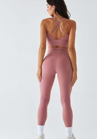 Biustonosz sportowy o wysokim stopniu wsparcia oraz dopasowane legginsy z miękkiego, fakturowanego materiału w kolorze różowego różu. Biustonosz ma krzyżujący się z tyłu design oraz szeroki pas w talii.
