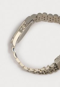 Hopea ruostumaton teräs -kello, jossa on linkitetty ranneke, teksturoitu reuna ja pyöreä kuori. Ranneke koostuu pyöreistä, päällekkäisistä linkeistä.