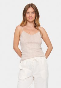 Beige ribitud tank top õhukeste rihmadega, V-kaelusega ja peene tekstuuriga. Kombineeritud kergest valgestest pükstest.