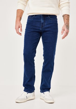 Dark blue denim jeans with a straight-leg cut, featuring five pockets, subtle stitching detail, and worn with white sneakers.
