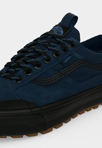 Μπλε αθλητικό παπούτσι Vans με μαύρα και μπλε κορδόνια, μαύρη καουτσούκ σόλα, καφέ πέλμα και χαρακτηριστική πλαϊνή ρίγα από σουέντ υλικό.