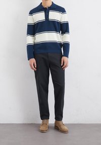 Polo a maniche lunghe a righe blu navy e bianche con tre bottoni, abbinato a pantaloni scuri e stivali alla caviglia color beige. Tessuto liscio.