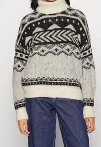 Stickad polotröja i kräm och svart, med geometriska mönster, rippade muddar och nederkant, samt en lös passform.