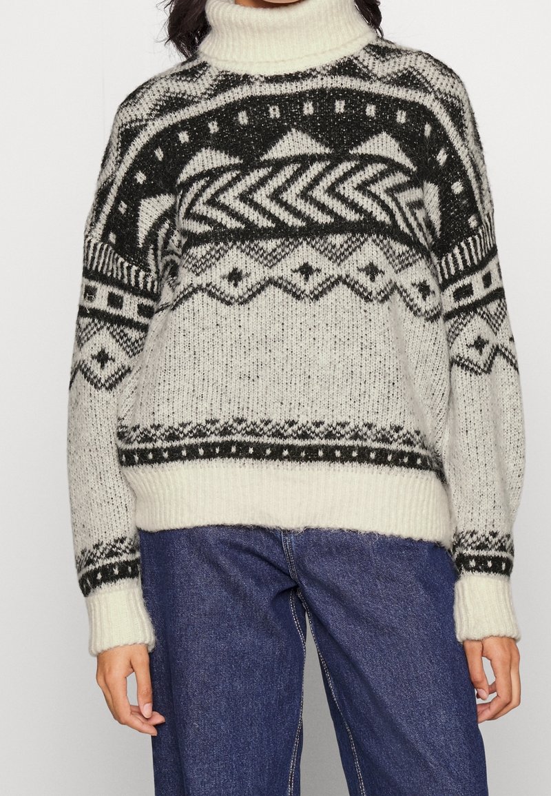 Stickad polotröja i kräm och svart, med geometriska mönster, rippade muddar och nederkant, samt en lös passform.