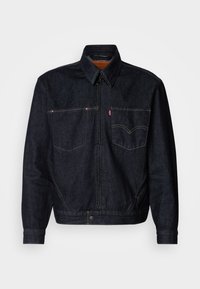 Temno modra denim jakna z zadrgo spredaj, dvema prsoma žepoma in ovratnikom. Ima kontrastno šivanje in označeno nalepko na levem žepu.