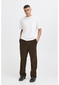 White short-sleeve t-shirt paired with dark brown corduroy pants and black shoes, standing on a plain white background.