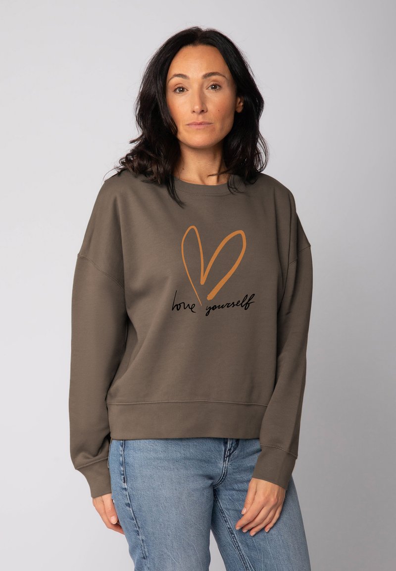 Bruine sweatshirts met een losse pasvorm, voorzien van een oranje hartgraphic en de tekst "hou van jezelf" in het zwart. Zacht, katoenmix materiaal.
