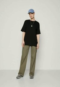 Black oversized t-shirt, loose olive pants, gray sneakers, and a light blue cap. Minimalist design with practical fit and neutral colors.