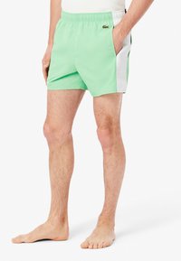 Shorts de bain verts en tissu léger. Comprend un panneau latéral blanc, une taille élastique et le logo Lacoste à l'avant.