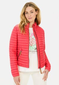 Rote gesteppte Jacke mit Reißverschluss vorne und Seitentaschen. Verfügt über einen Stehkragen und eine weiche Textur. Getragen über einem weißen Grafikshirt.