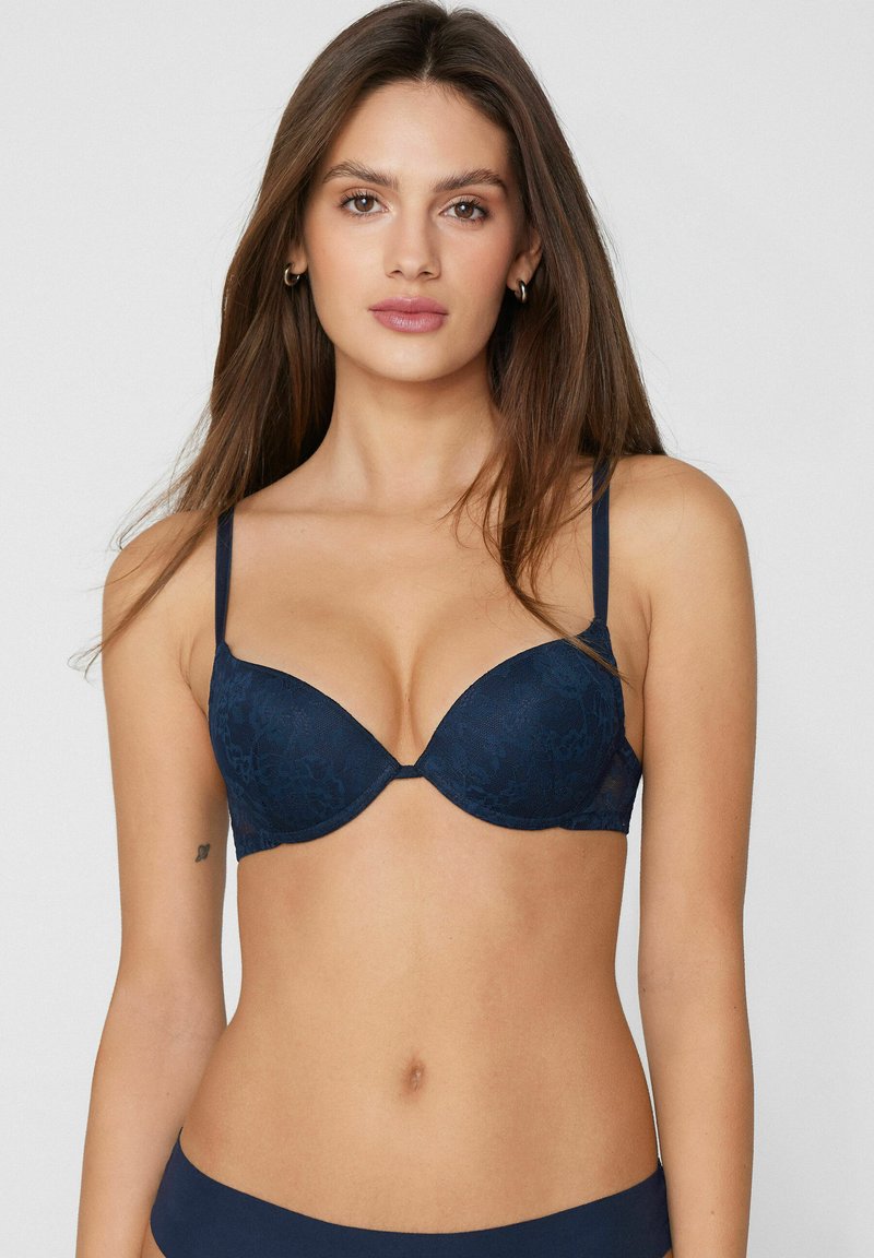 Marineblauwe kanten beha met gevormde cups en smalle verstelbare bandjes; heeft een gladde textuur en een bloemenpatroon over de stof.