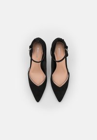 Zapatos de tacón alto de ante negro con punta afilada y tira en el tobillo, con un panel transparente en la parte delantera. Forro interior suave.