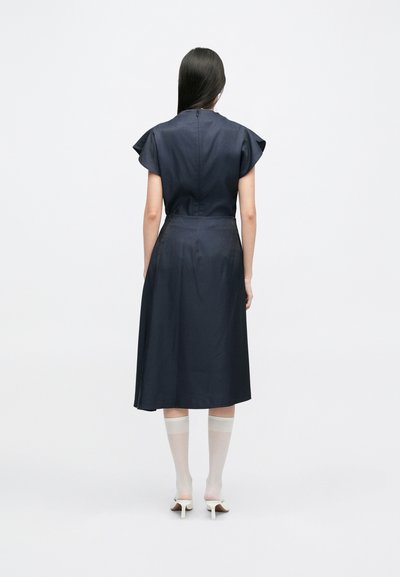 Mornarsko A-linijski oblek s kratkimi krilci, prilegajočim pasom in polno krilo. Gladka tkanina z diskretno bleščavostjo. Nosi se z prozornimi belimi nogavicami.