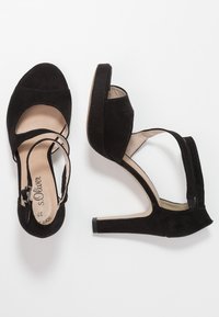 Svarta mocka högklackade skor med öppen tå och ankelsnodd. Har en slät sula och en blockklack för stabilitet.