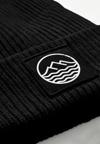 Black knitted beanie featuring a square woven patch with white mountain and wave graphic, highlighting texture and design details.