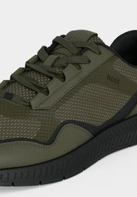 Baskets athlétiques vertes avec détails en mesh et cuir, semelle noire et lacets, marquées du logo "BOSS" sur le côté et la languette.