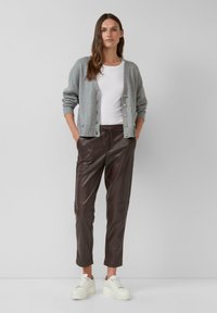 Grijze gebreide cardigan met gouden knopen, gecombineerd met bruine faux leren broeken en witte sneakers. De outfit heeft een relaxte pasvorm en een minimalistisch ontwerp.