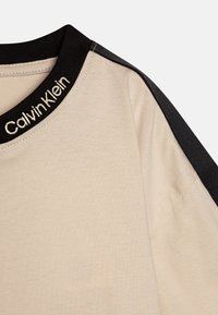 Beige Baumwollt-shirt mit einem schwarzen gerippten Kragen, auf dem "Calvin Klein" in Weiß gestickt ist, sowie schwarzen Akzenten an den Schulternähten.