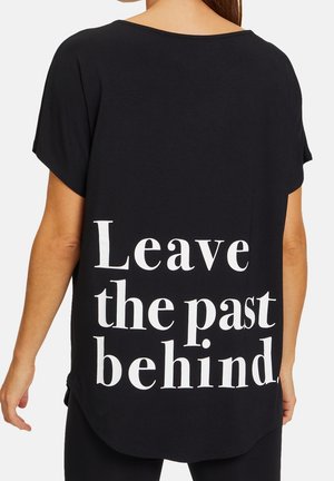 Czarna koszulka z krótkim rękawem z białym napisem na plecach „Zostaw przeszłość za sobą”, noszona przez osobę zwróconą tyłem do kamery.