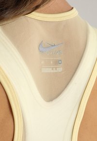 Camiseta atlética amarilla con espalda de malla y ribetes en contraste, que muestra un pequeño logo de Nike e información del producto.