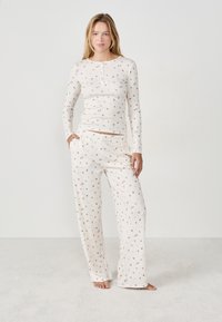Completo pigiama bianco composto da una maglietta a maniche lunghe con motivo floreale e pantaloni larghi abbinati, entrambi realizzati in un tessuto morbido.
