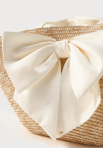 Sac à main en paille tressée avec un grand nœud en satin crème noué à l'avant, mettant en valeur la texture et un nœud décoratif élégant.