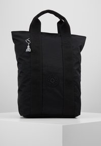 Zwarte stoffen draagtas met dubbele handvatten, voorzien van een ronde logopatch en een zilverkleurig sieraad bevestigd aan de zijkant.