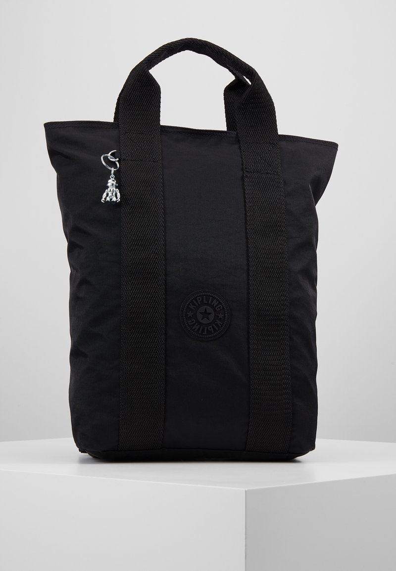 Zwarte stoffen draagtas met dubbele handvatten, voorzien van een ronde logopatch en een zilverkleurig sieraad bevestigd aan de zijkant.