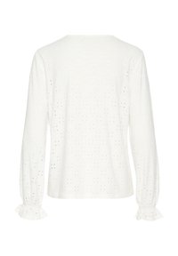 Blusa blanca de manga larga hecha de tela de ojal, con un cuello redondo, puños fruncidos y un patrón floral texturizado por toda la prenda.