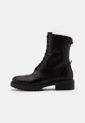 Bottine noire en cuir à lacets, semelle robuste et doublure en polaire blanche visible sur le bord supérieur, vue latérale sur fond blanc.