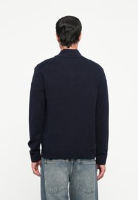 Navyblauer gestrickter Cardigan mit langen Ärmeln, geripptem Kragen und Saum. Verfügt über eine subtile Textur, eine normale Passform und keine sichtbaren Verschlüsse.