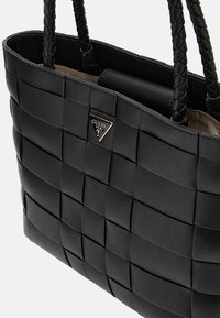 Zwarte geweven totebag met gevlochten handvatten en een zilveren driehoekig logo. Zachte lederen textuur met een gestructureerde vorm en een grote binnenkant.