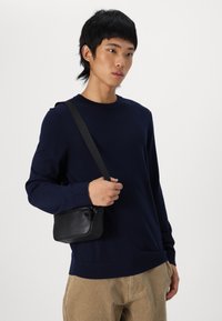 Dunkelblauer Pullover mit Rundhalsausschnitt und gerippten Bündchen, kombiniert mit einer kleinen schwarzen Lederumhängetasche mit Reißverschluss.