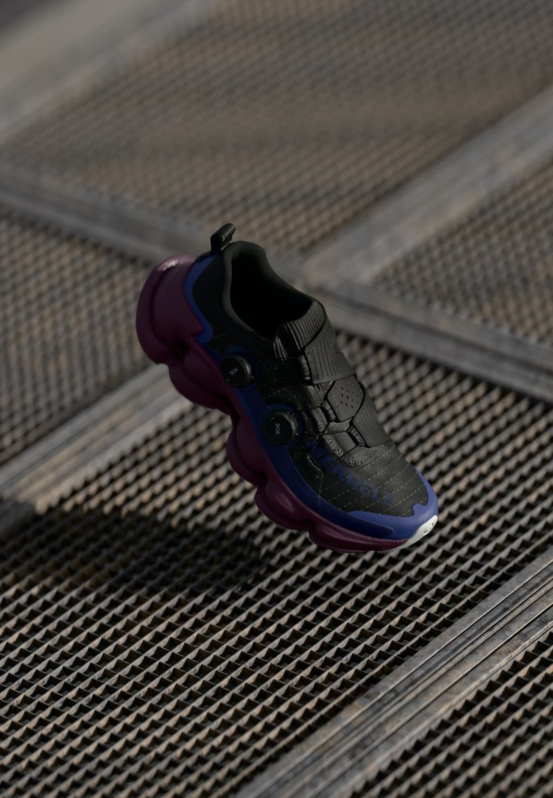 Black athletic shoe with purple and blue accents, textured upper, three adjustable straps, and a rounded sole design.