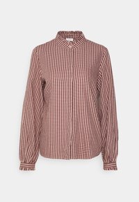 Chemise manches longues à motif vichy rouge et blanc, col montant à volants, poignets boutonnés et boutons dissimulés sur le devant, sur un fond uni.