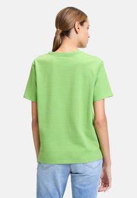 Zielona koszulka z krótkim rękawem, wykonana z teksturowanej tkaniny, z okrągłym dekoltem i luźnym krojem, w połączeniu z jasnoniebieskimi dżinsami.