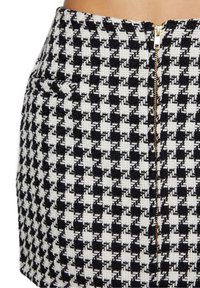 Jupe à motif pied-de-poule noir et blanc en tissu texturé, avec une fermeture éclair centrale dorée et des poches latérales.
