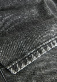 Tumši pelēks džinsu audums ar strukturētu austu. Satur redzamus šuvi un kontrastējošu svītru rakstu gar malu.