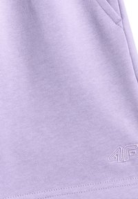 Gros plan d'un vêtement violet clair avec détail de poche cousu et un petit logo 4F brodé près de l'ourlet.