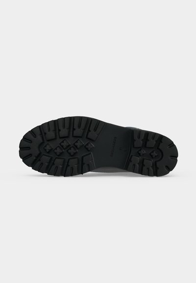 Semelle de bottes en caoutchouc noir avec des motifs de bande de roulement profonds conçus pour l'adhérence et la durabilité sur fond gris clair.