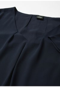 Granatowa bluzka z dekoltem w kształcie litery V, detalem w postaci zakładek na biuście i krótkimi rękawami; wykonana z gładkiej, lekkiej tkaniny.