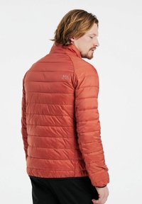 Giacca rossa imbottita con colletto alto, caratterizzata da sezioni trapuntate orizzontali e un piccolo logo sulla spalla sinistra. Tessuto morbido e leggero.