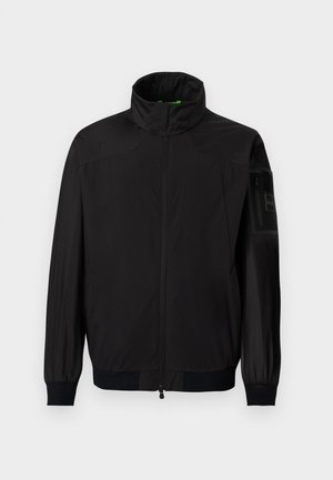 Μαύρο ελαφρύ μπουφάν με ψηλό γιακά, ολόκληρο φερμουάρ μπροστά, ελαστικά μανσέτα και τσέπη με φερμουάρ στο πάνω μέρος του αριστερού μανικιού.