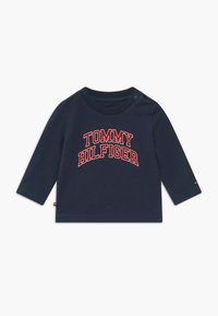 Námořnická dlouhá rukávová košile pro batolata vyrobená z bavlny, s nápisem "TOMMY HILFIGER" velkými červenými a bílými písmeny na přední straně. Zapínání na patentky na rameni.