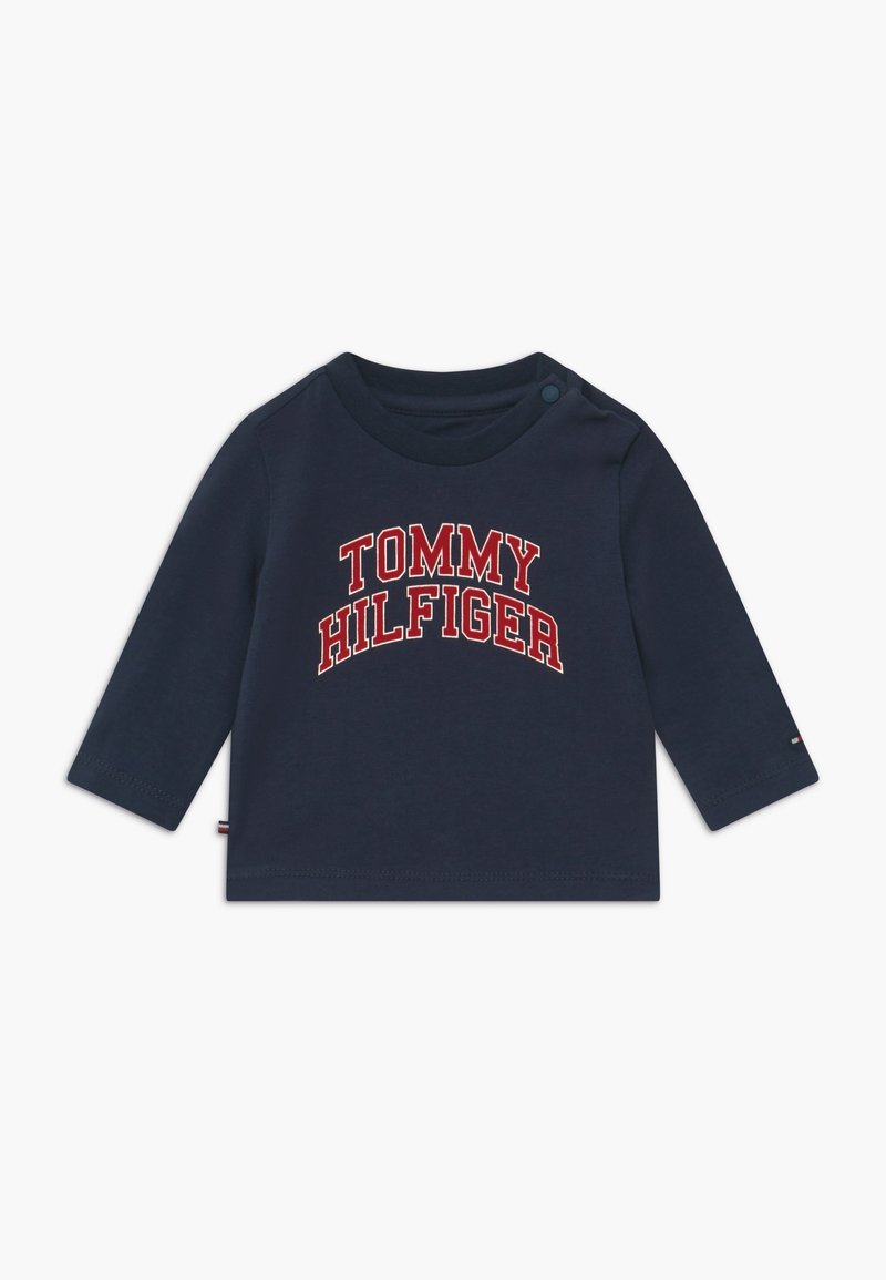 Námořnická dlouhá rukávová košile pro batolata vyrobená z bavlny, s nápisem "TOMMY HILFIGER" velkými červenými a bílými písmeny na přední straně. Zapínání na patentky na rameni.