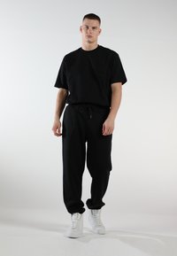 Schwarzes Baumwoll-T-Shirt und passende Sweatpants mit elastischem Bund, kombiniert mit weißen Sneakern. Einfaches Design, entspannte Passform und glatte Textur.