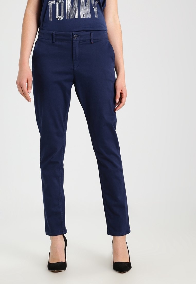 Femme portant un pantalon slim bleu marine, des talons hauts noirs et un haut bleu marine avec le texte "TOMMY".